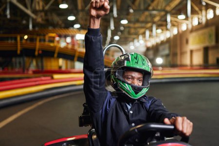 Foto de Go kart speed drive carrera indoor, emocionado piloto afroamericano en casco celebrando la victoria - Imagen libre de derechos