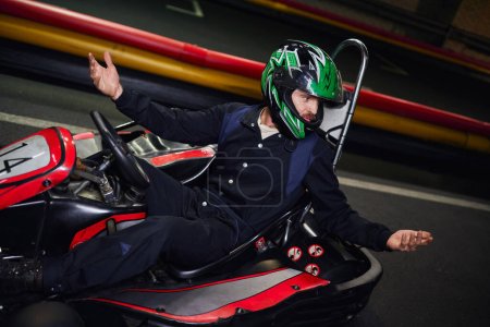 Emotionaler Fahrer mit Helm gestikuliert beim Kart-Fahren auf Indoor-Rundkurs