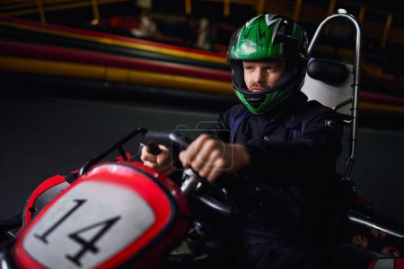 man in helmet and sportswear driving go kart on indoor circuit, adrenaline and motorsport concept