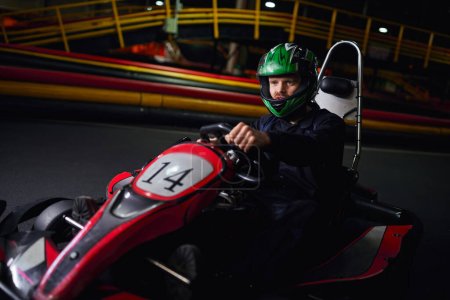 Rennfahrer in Helm und Sportbekleidung fahren Go-Kart auf Indoor-Rundkurs, Adrenalin- und Motorsport-Konzept