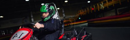 piloto enfocado en casco y ropa deportiva de conducción ir kart en circuito interior, concepto de adrenalina, bandera