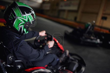 Rennfahrer in Helm und Sportbekleidung fahren Go-Kart auf Indoor-Rundkurs, Adrenalin- und Motorsport-Konzept