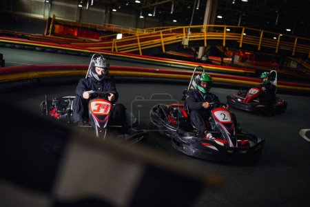 Photo for Diverse men driving go kart near checkered black and white racing flag on blurred foreground - Royalty Free Image