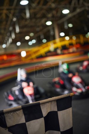 checkered black and white racing flag next to drivers on blurred backdrop, go kart concept
