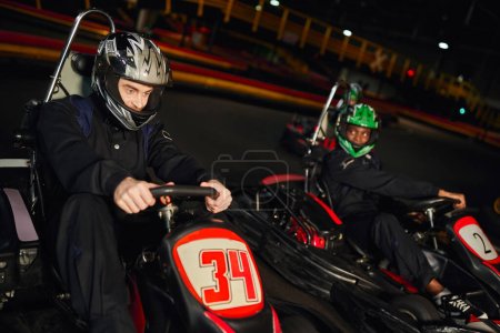 focused multiethnic people driving go kart car on indoor circuit, speed racing and competition