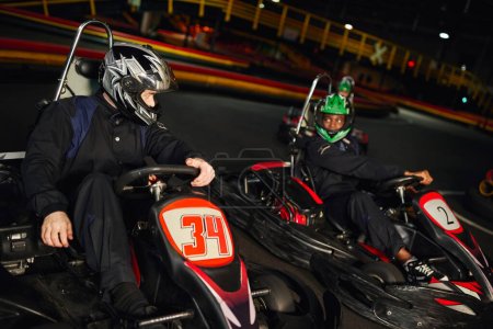 competidores multiétnicos conducir ir kart en circuito cubierto, carreras de velocidad y automovilismo