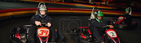 Photo for Focused multicultural go cart racers driving on indoor circuit, speed racing and motorsport, banner - Royalty Free Image