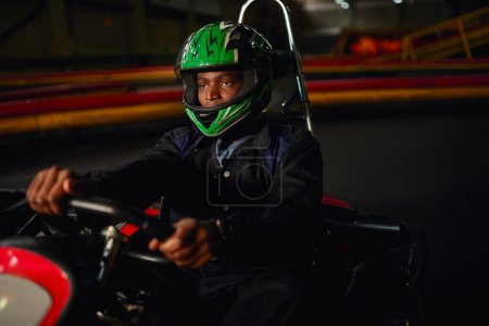 african american go kart driver in helmet driving on indoor circuit, speed racing challenge