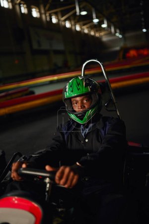 afrikanisch-amerikanischer Go-Kart-Fahrer mit Helm auf Indoor-Rundkurs, Speed-Rennstrecke, Motorsport