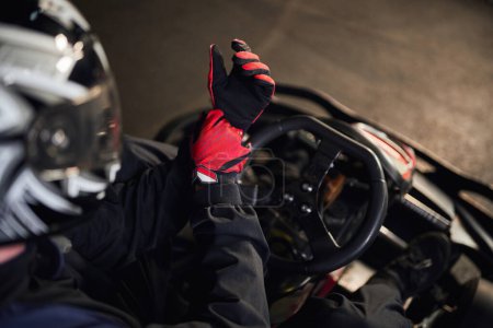 top view of go kart racer in helmet wearing red sport gloves, preparing for competition concept