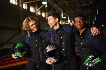 groupe de coureurs de karting multiculturels et heureux go en combinaisons de protection étreignant et tenant des casques