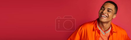 excited african american guy laughing on red background, orange shirt, portrait, banner, copy space