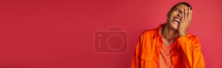 Foto de Chico afroamericano emocionado riendo y oscureciendo la cara en rojo, camisa naranja, pancarta, espacio de copia - Imagen libre de derechos