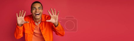 funny african american guy showing scary gesture and grimacing on red, orange shirt, banner