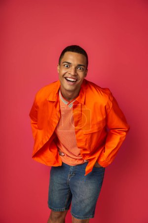 overjoyed and funny african american man, crazy face expression looking at camera on red background