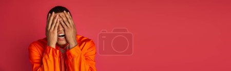 Foto de Hombre afroamericano trastornado en camisa naranja que oscurece la cara con las manos en rojo, pancarta, espacio de copia - Imagen libre de derechos