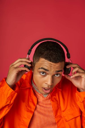 stilvoller afrikanisch-amerikanischer Mann, der Musik in drahtlosen Kopfhörern auf rotem Hintergrund hört
