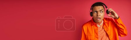 Téléchargez les photos : Surpris homme afro-américain en casque sans fil et chemise orange sur rouge, bannière, espace de copie - en image libre de droit