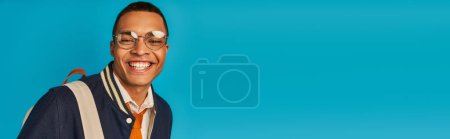 happy african american student in stylish jacket and eyeglasses on blue, banner, copy space
