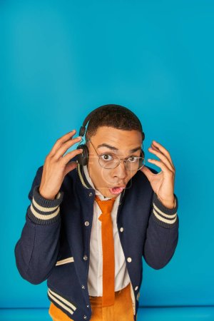 Photo for Astonished african american student in headphones, with open mouth looking at camera on blue - Royalty Free Image