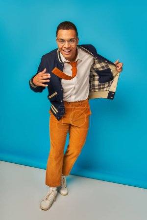 confident african american student with trendy clothes and radiant smile looking at camera on blue