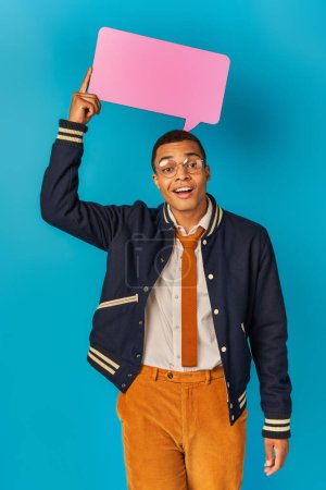 Foto de Estudiante afroamericano sonriente en chaqueta de moda y gafas que sostienen la burbuja del habla en azul - Imagen libre de derechos