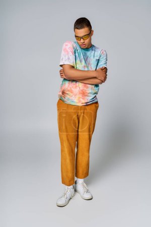 Téléchargez les photos : Homme afro-américain à la mode avec les mains pliées sur le gris, t-shirt tie-dye, pantalon orange, lunettes de soleil - en image libre de droit