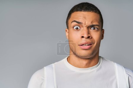young and discouraged african american in trendy t-shirt looking at camera on grey