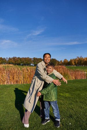 Foto de Vinculación, naturaleza otoñal, madre afroamericana feliz abrazando al hijo, familia en ropa de abrigo, caída - Imagen libre de derechos