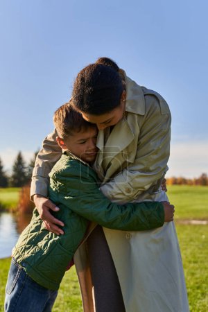 african american woman hugging son, calming, standing near lake in park, african american family