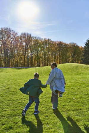 sunny day in fall, african american woman running together with son in park, grass, autumnal fashion