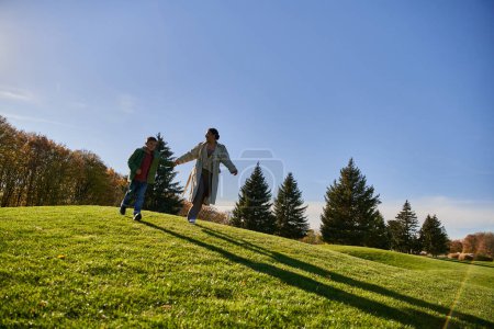 sunny day in autumn, happy african american woman running together with son in park, candid