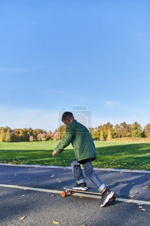 Foto de Lindo niño en ropa de abrigo a caballo penny board, asfalto, parque, temporada de otoño, niño en ropa otoñal - Imagen libre de derechos