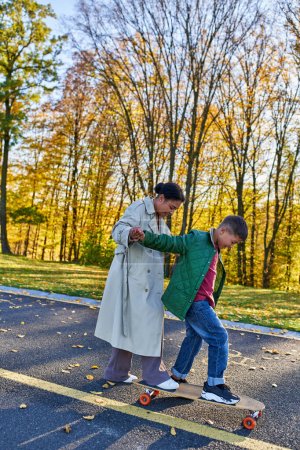 Photo for Mother and son, bonding, autumn, happy african american woman holding hands with boy on penny board - Royalty Free Image