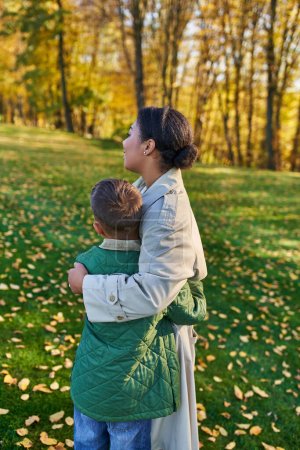 Mutterliebe, Rückansicht, afrikanisch-amerikanische Frau umarmt niedlichen Sohn, steht neben goldenen Blättern