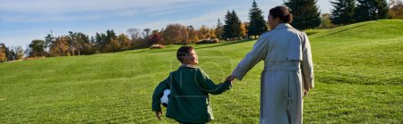 Photo for African american boy holding football, walking with mom on green field, holding hands, fall, banner - Royalty Free Image