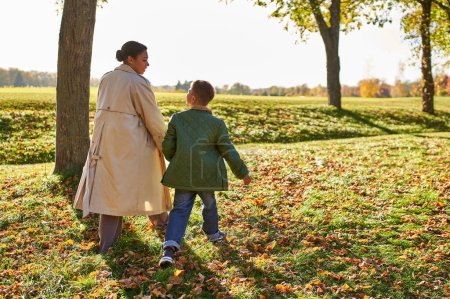 Photo for Golden hour, mother and son walking in park, autumn leaves, fall season, african american family - Royalty Free Image