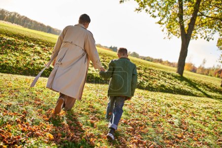 Photo for Golden hour, mother and son walking in park, hold hands, autumn leaves, fall, african american - Royalty Free Image
