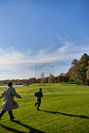 candid shot, african american mother and son running on green grass, having fun, autumn outerwear