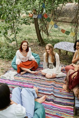 Photo for Joyful multiethnic women in stylish outfits spending time on lawn outdoors in retreat center - Royalty Free Image