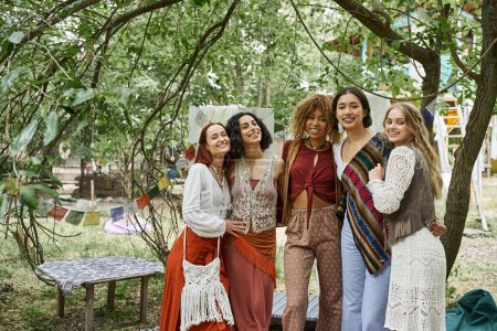 positive and multiethnic women in boho outfit looking at camera in retreat center