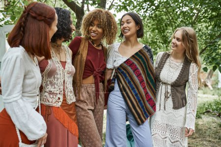 cheerful and stylish interracial group of women hugging outdoors in retreat center