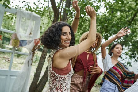 positive multicultural woman looking at camera while dancing near friends in retreat center