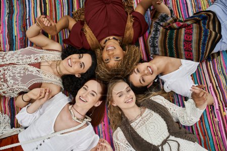top view of cheerful interracial women looking at camera on blanket in retreat center