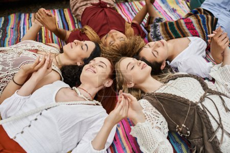 mujeres multiétnicas alegres con los ojos cerrados cogidos de la mano, manta, al aire libre, centro de retiro