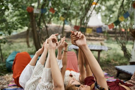multiethnic women raising and holding hands while lying together outdoors in retreat center