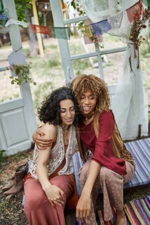 smiling african american woman hugging multicultural friend outdoors in retreat center