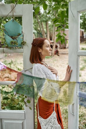 beautiful redhead woman in boho outfit standing near door outdoors in retreat center
