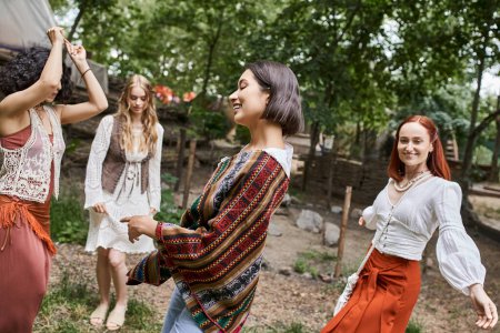 Photo for Positive brunette woman in stylish outfit dancing near multiethnic friends in retreat center - Royalty Free Image