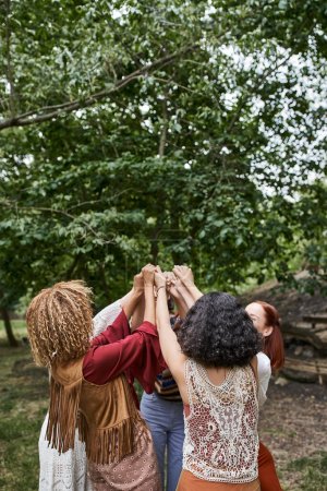 trendige multiethnische Freundinnen in Boho-Klamotten, die sich draußen im Retreat Center die Hände reichen